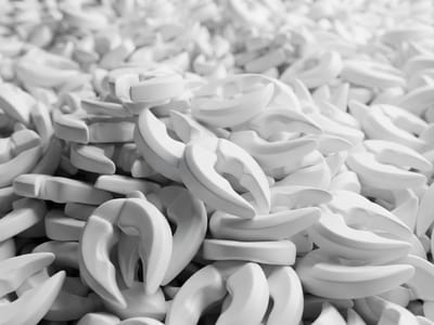 A dense pile of identical white curved claw-like plastic objects with shallow depth of field.